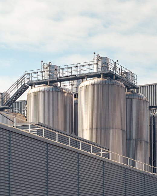 A view of metal storage tanks outside an industrial facility under a partly cloudy sky.